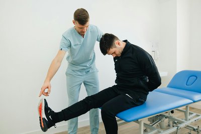 Slika terapevtka, ki drži prste na stopalih moškega, ki sedi in gleda navzdol