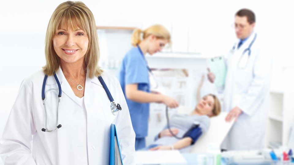A symbolic image of a female doctor in the foreground, while in the background there is a patient lying on a bed, while the nurse and the doctor are observing her.
